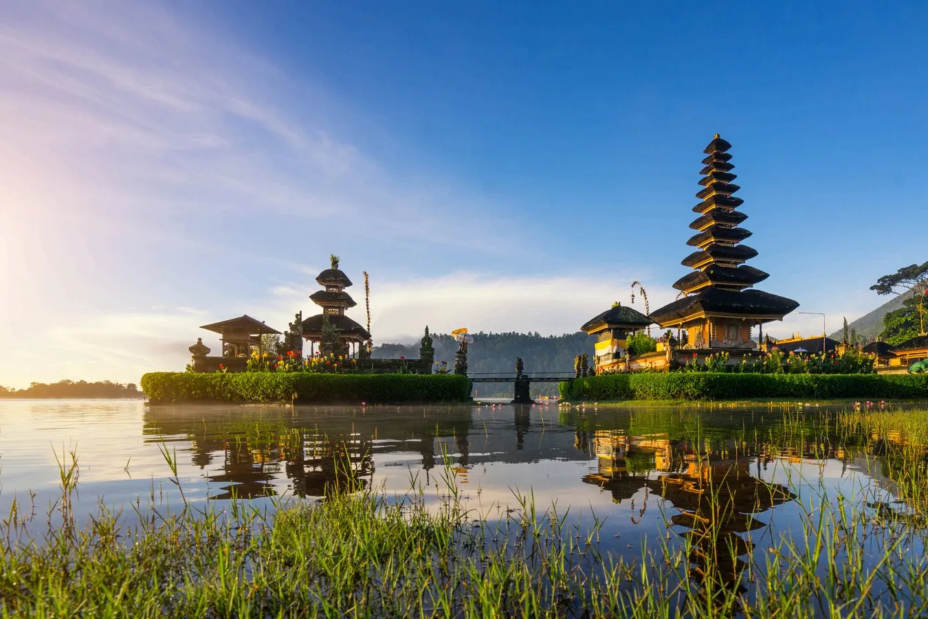 El templo de Ulun Danu Beratan a orillas del lago, con su torre de tejados escalonados de paja reflejada en el agua y los jardines del recinto delante.