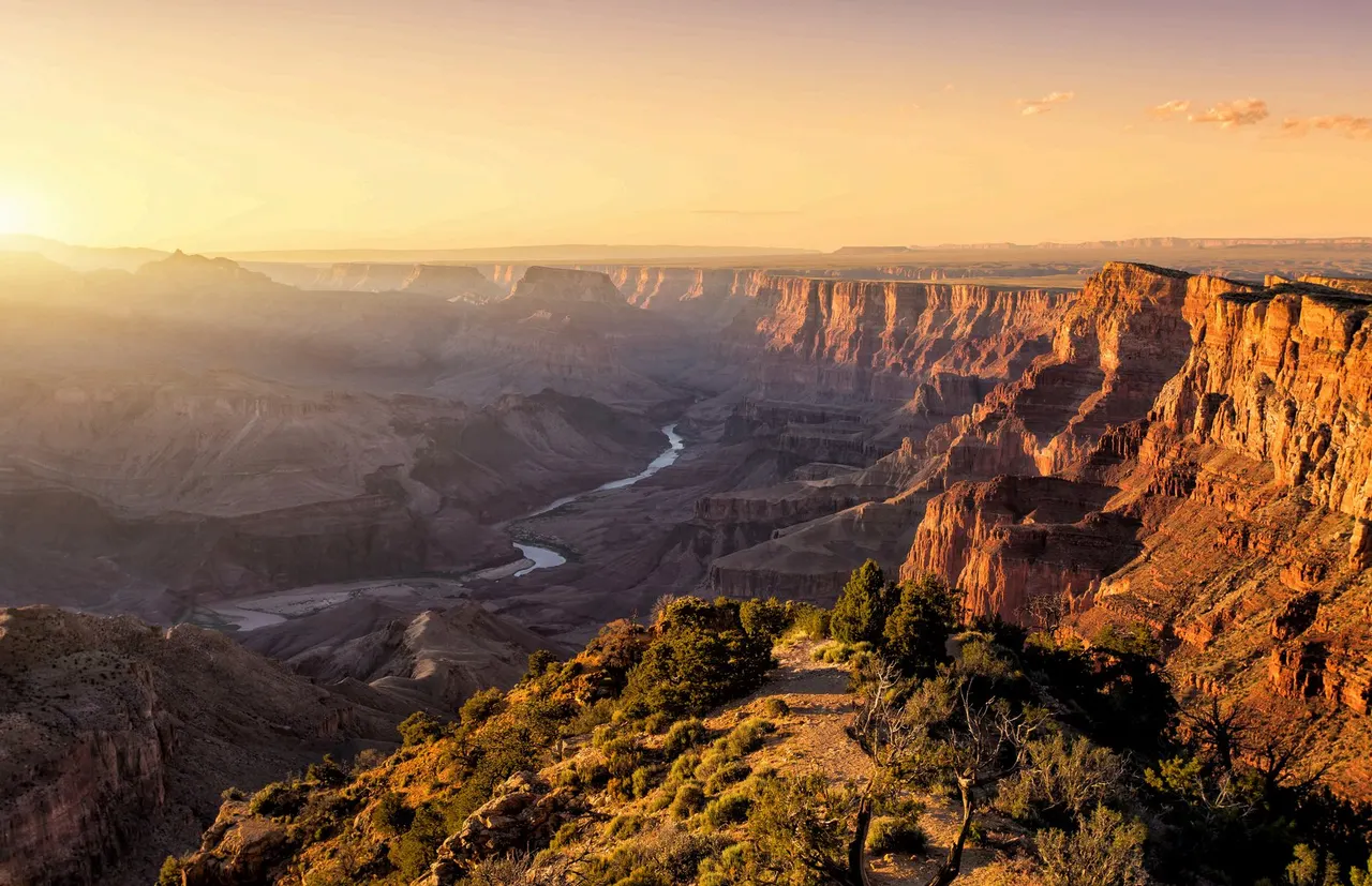 El Gran Cañón del Colorado al atardecer, con el río abriéndose paso en el fondo del cañón y la luz rasante sobre las paredes de roca.