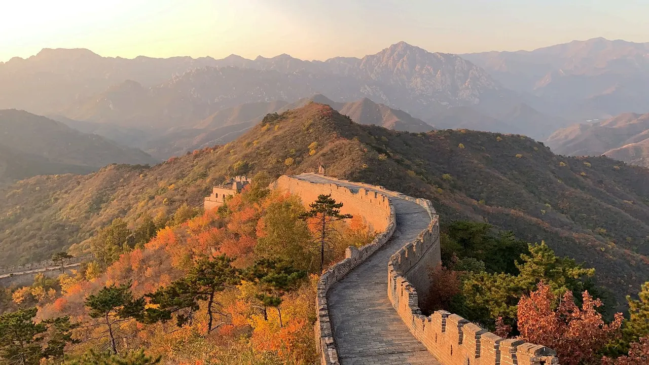 Un tramo de la Gran Muralla China serpenteando por la cresta de las montañas, con las torres de vigilancia y las laderas cubiertas de vegetación otoñal.