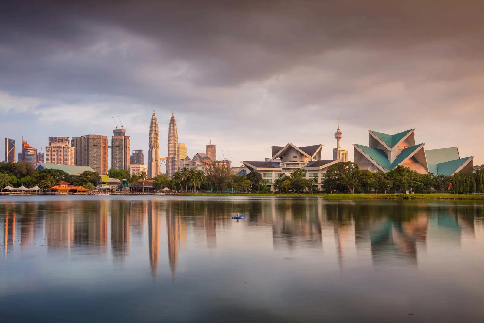 El perfil de Kuala Lumpur al atardecer visto desde un lago, con las Torres Petronas y la torre de comunicaciones reflejadas en el agua en calma.