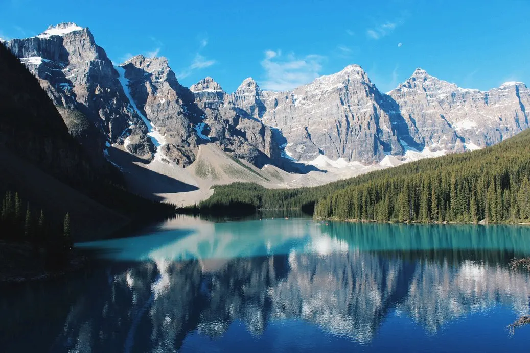 El lago Moraine, de agua turquesa, al pie del valle de los Diez Picos, con las cumbres nevadas y el bosque de coníferas reflejados en la superficie.