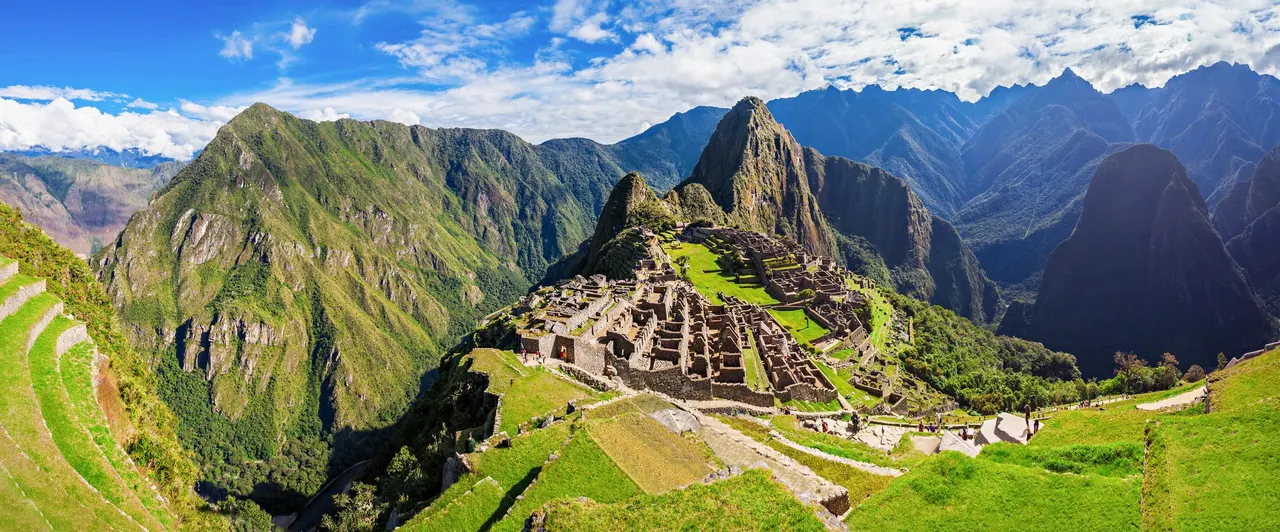 Panorámica de la ciudadela de Machu Picchu con sus terrazas y recintos de piedra, el Huayna Picchu detrás y las montañas verdes del valle al fondo.