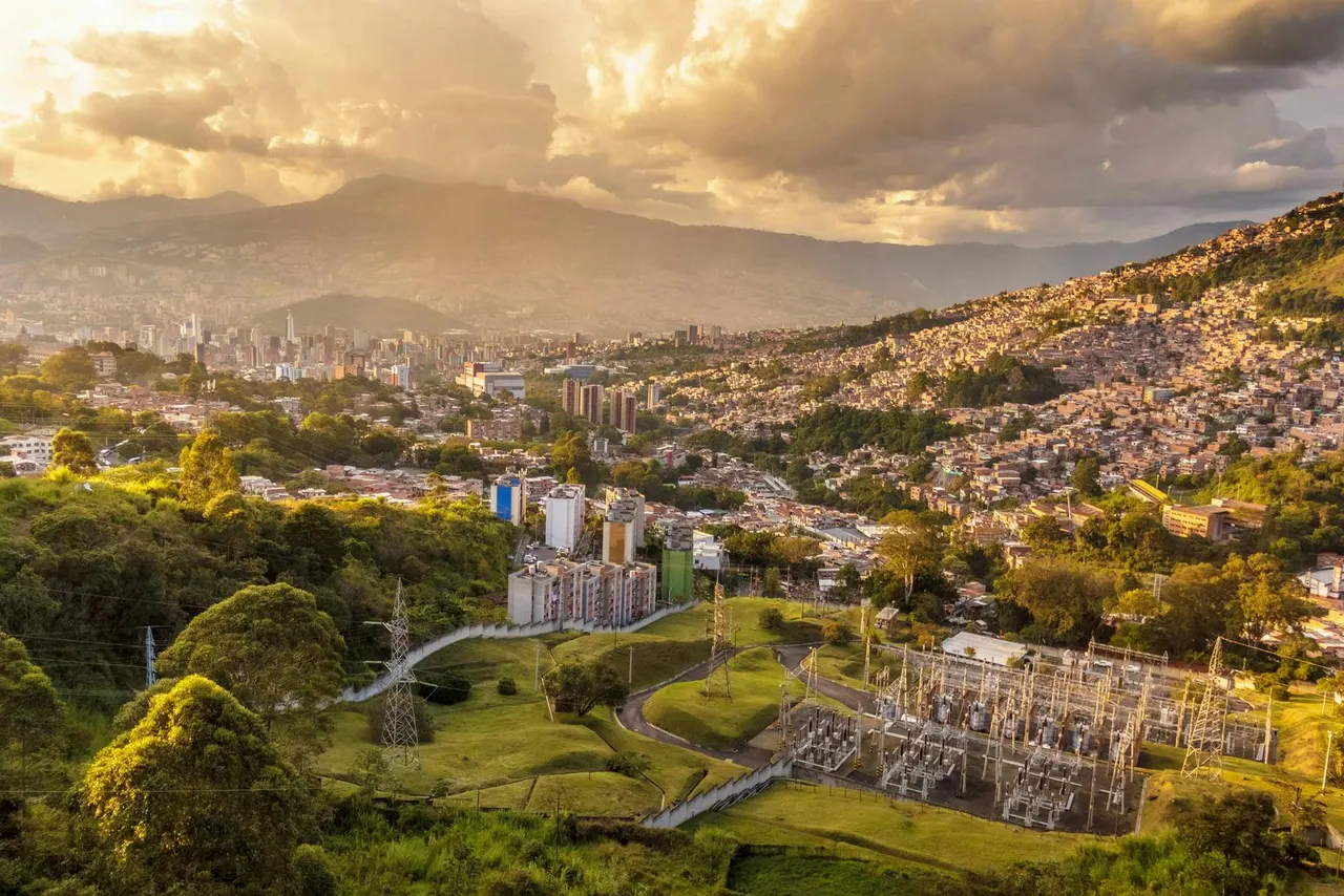El valle de Medellín al atardecer, con los barrios trepando por las laderas verdes y la ciudad al fondo bajo las montañas.