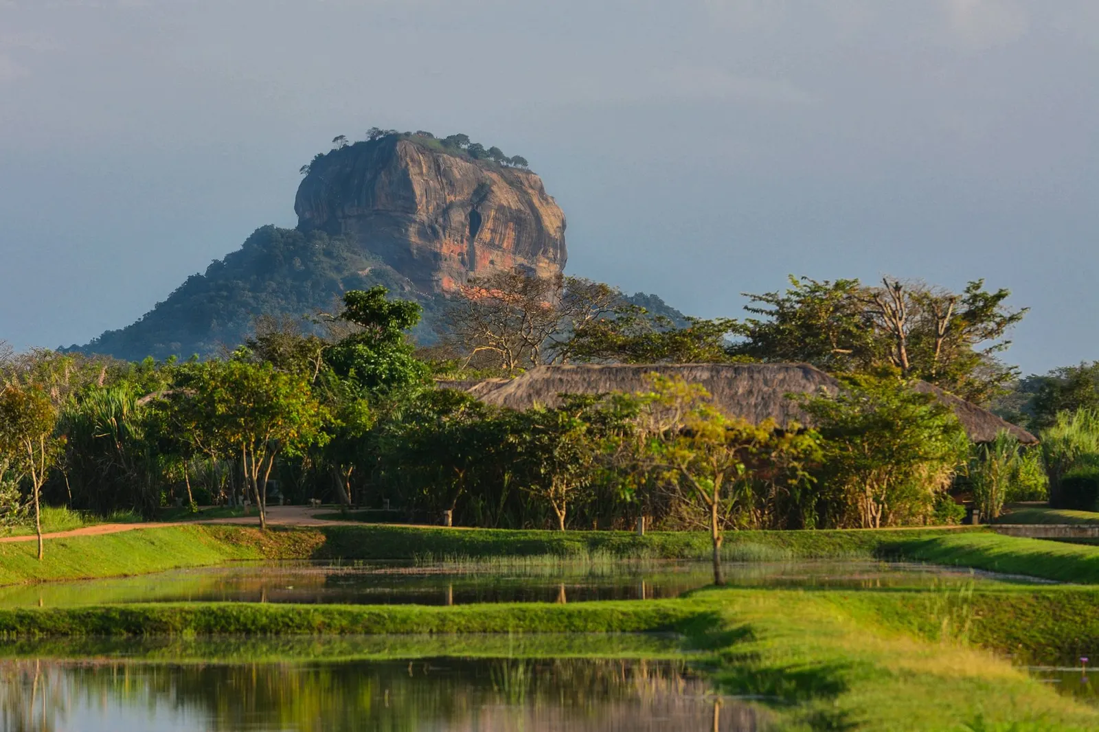 La roca de Sigiriya alzándose sobre la selva de Sri Lanka, con su pared vertical de piedra rojiza y la vegetación cubriendo la llanura alrededor.