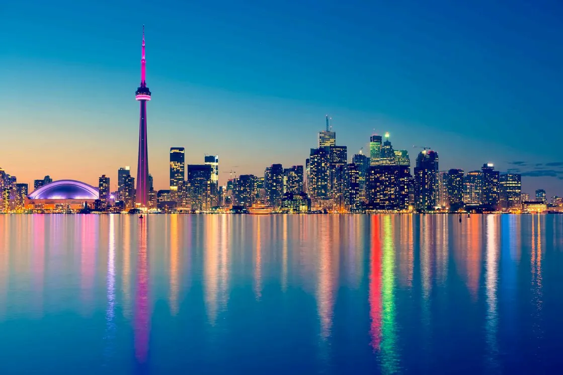 El perfil de Toronto de noche desde el lago Ontario, con la torre CN iluminada y las luces de los rascacielos reflejadas en el agua.