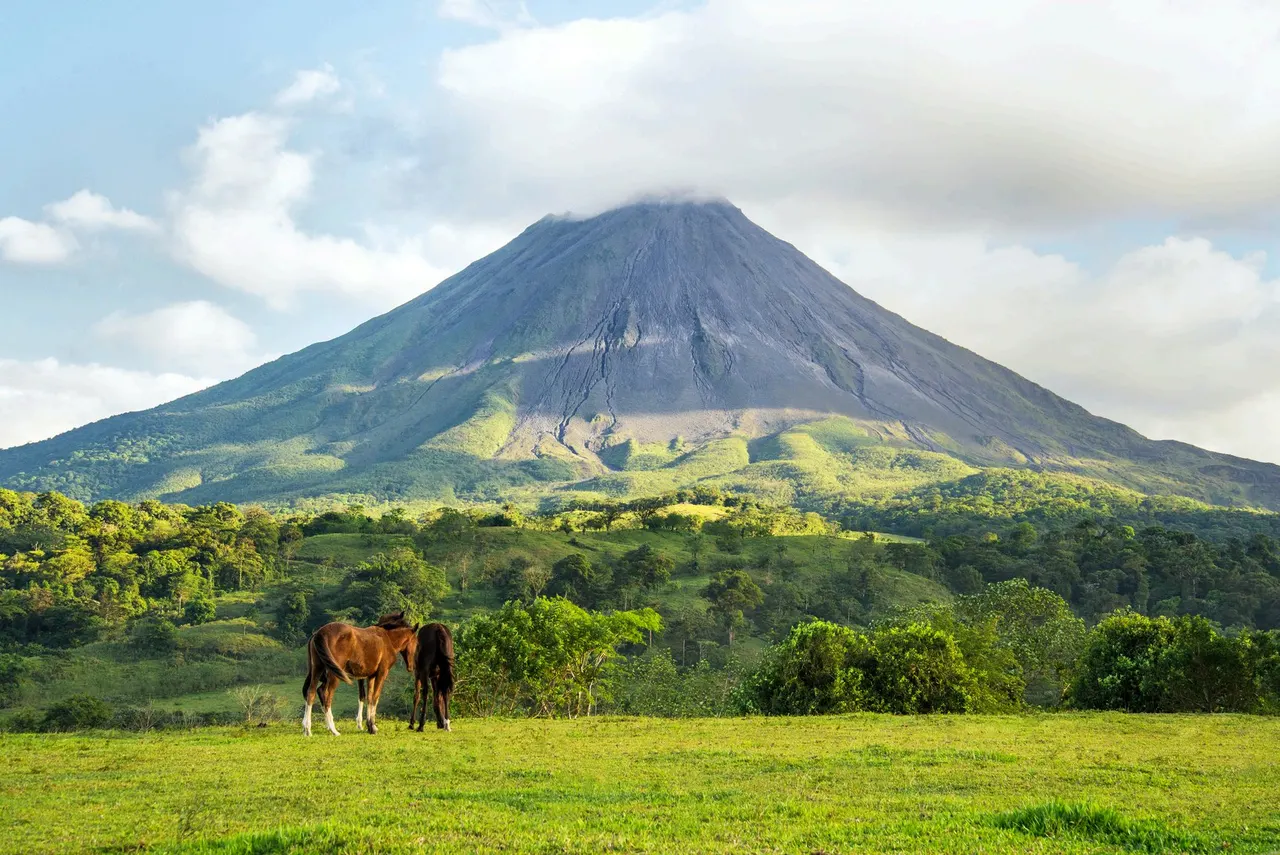 El cono del volcán Arenal alzándose sobre la selva tropical, con la cima entre nubes y la ladera cubierta de vegetación densa.