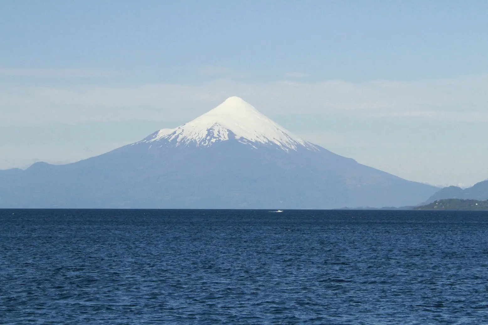 El volcán Osorno con la cima nevada, visto desde la otra orilla de un lago de aguas azul oscuro en un día despejado.